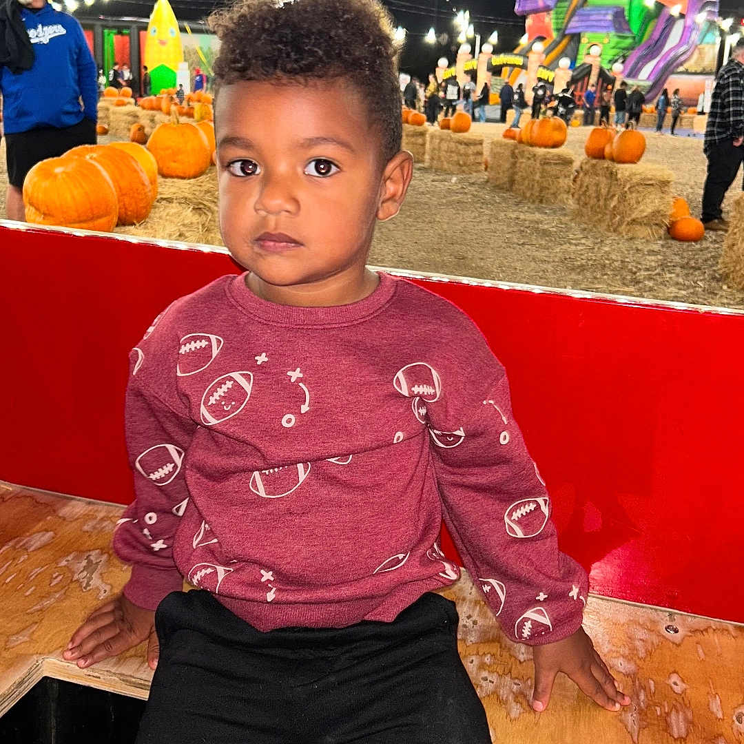 Jeffer is registered to the contest to win money with this photo: bench, casual, child, clothing, event, fall, festival, football_pattern, hay_bales, inflatable_slide, night, outdoor, pants, people, pumpkin_patch, pumpkins, serious, spiderman, string_lights, wood