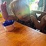 toddler, child, cupcake, purple_frosting, wooden_table, smile, happy, indoor, sunlight, window, chair, celebration, food, birthday, person, clothing, hair, face, hands, home