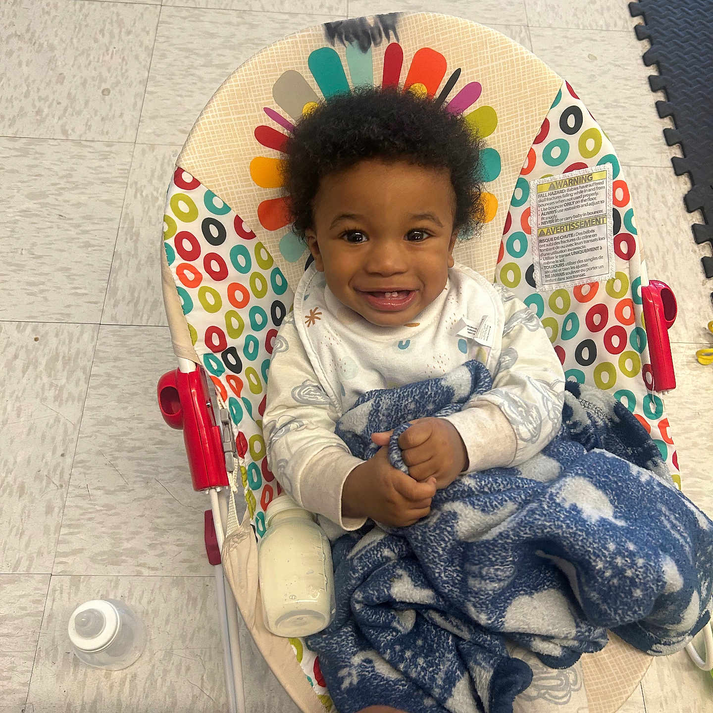 Kajun joined the competition — help win amazing prizes! baby, baby_bottle, baby_chair, blanket, blanket_pattern, bottle, child, clothing, colorful, curly_hair, floor, floor_tiles, happy, indoor, infant, patterned, person, seat, smiling, toy