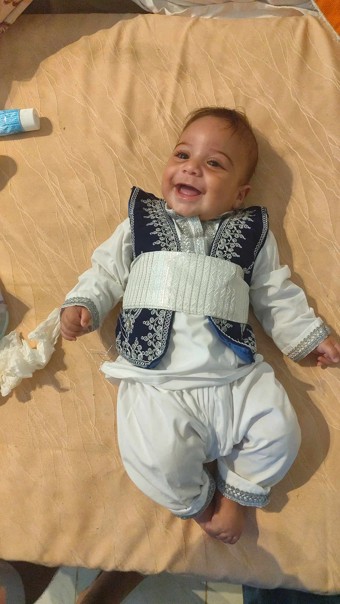 Adam participe au concours pour gagner de l'argent avec cette photo : baby, smiling, lying_down, traditional_clothing, embroidery, blanket, indoors, tissue, tube, happy, child, person, foot, hand, fabric, cute, portrait, infant, clothing, relaxed