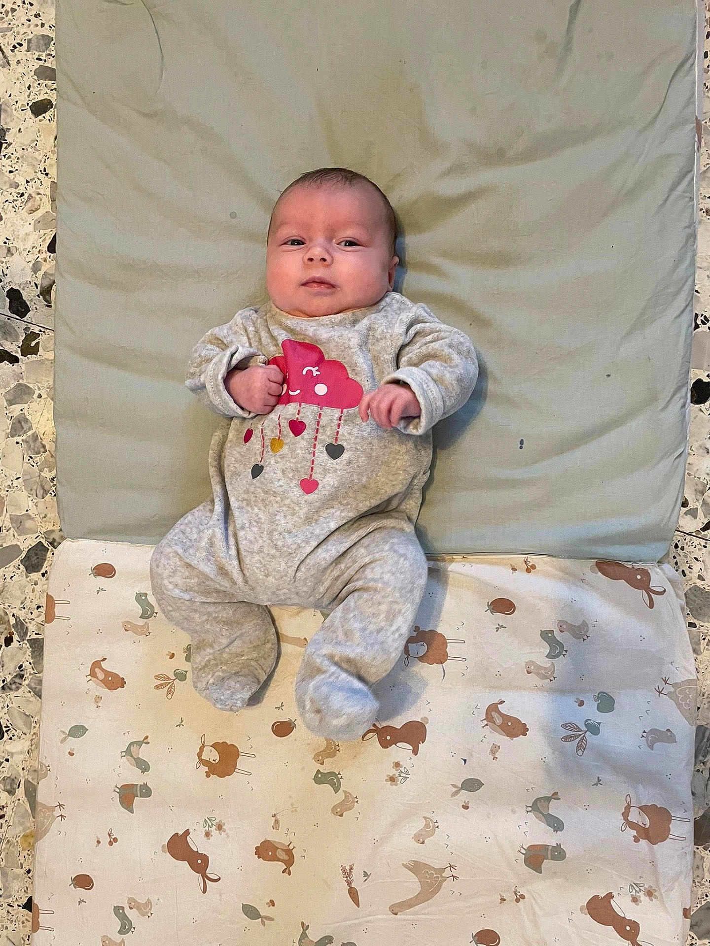 Ambre a rejoint le concours — aidez-le/la à gagner de superbes lots ! baby, infant, onesie, clothing, blanket, cushion, floor, pattern, animal_print, face, person, lying_down, cute, indoor, newborn, baby_garment, expression, comfort, soft_texture, small_hands