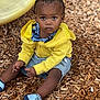 toddler, child, yellow_hoodie, braids, blue_shoes, wood_chips, outdoor, serious_expression, sitting, playground, curious, casual_clothing, shorts, portrait, daylight, person, young_child, closeup, natural_light, cute