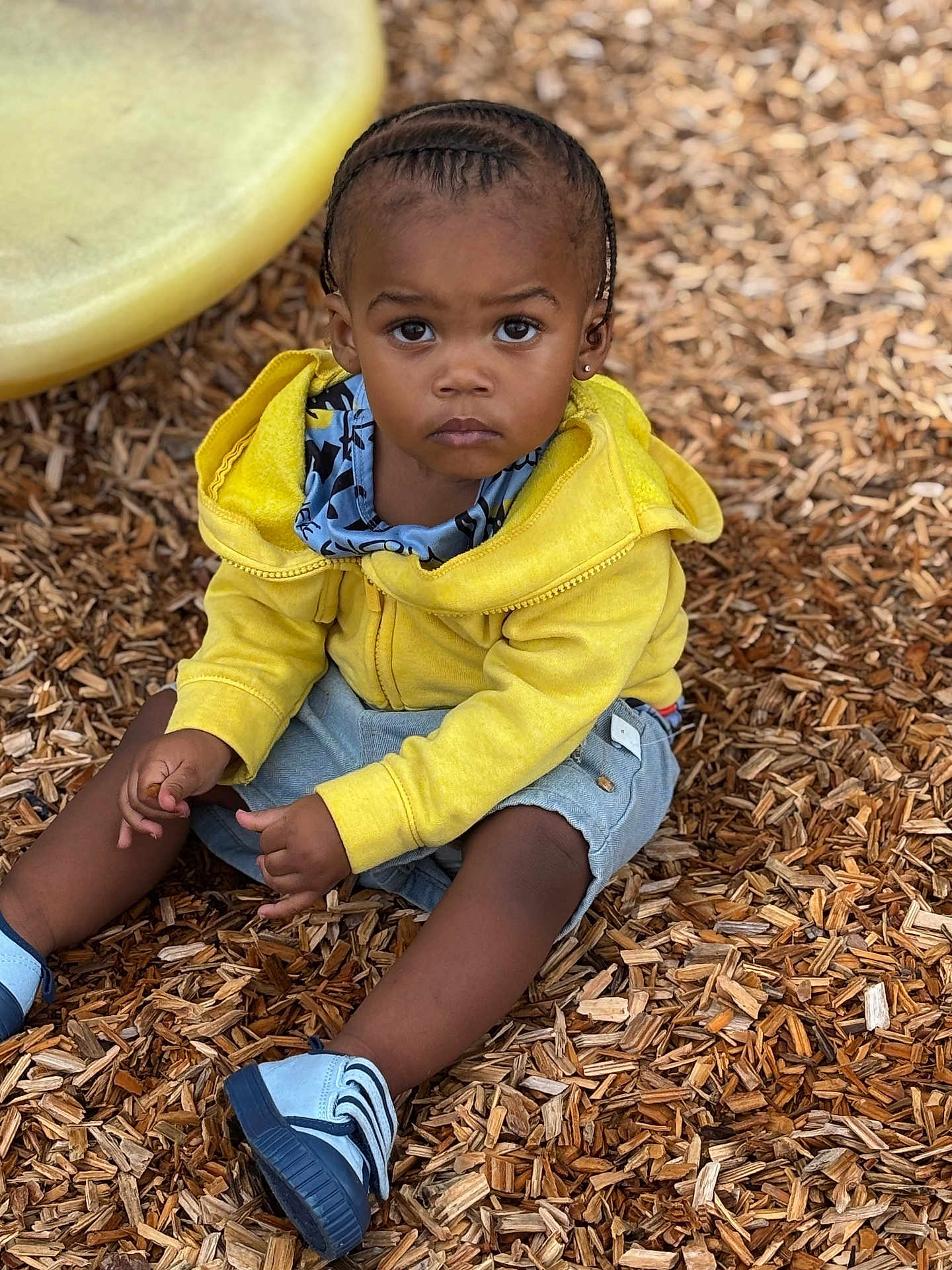 Jayceveon joined the competition — help win amazing prizes! toddler, child, yellow_hoodie, braids, blue_shoes, wood_chips, outdoor, serious_expression, sitting, playground, curious, casual_clothing, shorts, portrait, daylight, person, young_child, closeup, natural_light, cute