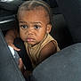 child, toddler, car, car_seat, bottle, braided_hair, earring, curious, brown_skin, clothing, seatbelt, interior, vehicle, person, portrait, looking, sitting, young_child, indoors, expression