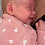 baby, infant, smiling, sleeping, pink_clothing, hearts_pattern, close_up, snuggling, skin, face, person, love, comfort, tenderness, newborn, cuddling, family, parent, warmth, gentle