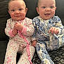 baby, infant, child, pajamas, floral_pattern, couch, smiling, happy, indoors, cute, sitting, two_children, face, hands, footed_pajamas, light_skin, blue_eyes, pink, blue, cozy