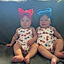baby, infant, twin, headband, bow, red_bow, blue_bow, couch, sitting, cute, outdoor_light, patterned_clothing, legs, feet, portrait, child, two_people, indoor, expression, face