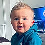 baby, blue_eyes, casual, child, clothing, curly_hair, cute, face, furniture, home, hoodie, indoor, living_room, person, portrait, seated, smiling, television, toddler, young_child