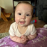 Jazlyn joined the competition — help win amazing prizes! baby, infant, child, blanket, purple_blanket, indoor, wooden_floor, toy, furniture, smiling, hands, face, cute, curious, eyes, short_hair, onesie, propped_up, floor, cozy