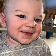 Marceau S a rejoint le concours — aidez-le/la à gagner de superbes lots ! child, baby, infant, toddler, smile, blue_eyes, rosy_cheeks, blonde_hair, face, ear, closeup, portrait, gray_shirt, text_on_clothing, drooling, indoor, dining_room, chair, background_bokeh, happy