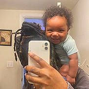 Tyus joined the competition — help win amazing prizes! baby, child, adult, mirror, selfie, smartphone, dreadlocks, smile, indoor, wall, light_switch, doorway, clothing, hand, portrait, person, hair, room, happy, casual