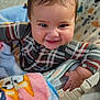 baby, infant, smiling, grinning, cheeks, plaid_onesie, blanket, soft_blanket, highchair, hand, fingers, hair, eyes, indoors, close_up, portrait, playful, patterned_mat, cozy, nursery
