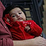 Anette is registered to the contest to win money with this photo: baby, infant, child, red_clothing, person, arm, hand, face, expressionless, indoor, holding, closeup, portrait, sleepy, cozy, soft_lighting, blurred_background, adult, resting, warmth