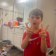 Ty Sears is registered to the contest to win money with this photo: child, boy, red_shirt, peace_sign, bathroom, mirror, cabinet, floor, lighting, expression, clutter, clothing, person, indoor, hand_gesture, reflection, countertop, plastic_container, wood_floor, casual
