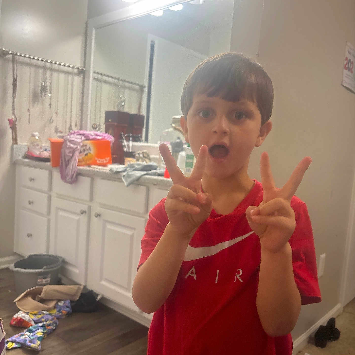 Ty Sears is registered to the contest to win money with this photo: bathroom, boy, cabinet, casual, child, clothing, clutter, countertop, expression, floor, hand_gesture, indoor, lighting, mirror, peace_sign, person, plastic_container, red_shirt, reflection, wood_floor