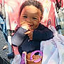 baby, smiling, stroller, blanket, toy, teether, curly_hair, outdoor, sunlight, happy, child, clothing, person, infant, seat, rainbow_pattern, playful, cute, warm_clothes, daylight