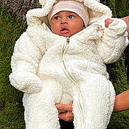 Ivy participe au concours pour gagner de l'argent avec cette photo : baby, child, infant, white_onesie, fluffy_clothing, hat, beige_hat, tree_bark, moss, outdoor, nature, person, cute, warm_clothing, hands, portrait, expression, young_child, holding, winter_wear