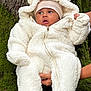 baby, child, infant, white_onesie, fluffy_clothing, hat, beige_hat, tree_bark, moss, outdoor, nature, person, cute, warm_clothing, hands, portrait, expression, young_child, holding, winter_wear