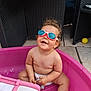 toddler, child, goggles, swimming_goggles, pink_tub, toy, outdoor, patio, plastic, happy, smiling, curly_hair, bare_chest, diaper, summer, playtime, yellow_ball, wicker_chair, concrete_floor, cute
