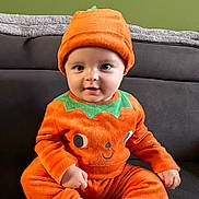 Léon participe au concours pour gagner de l'argent avec cette photo : baby, child, pumpkin_costume, orange_clothing, hat, cute, smiling, sitting, indoor, couch, green_wall, face, portrait, infant, cozy, seasonal, festive, happy, person, costume