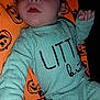 baby, infant, child, clothing, green_outfit, blanket, orange_blanket, jack_o_lantern, pumpkin_pattern, face, hand, lying_down, cute, expression, indoors, portrait, young_child, sleepwear, fabric, person