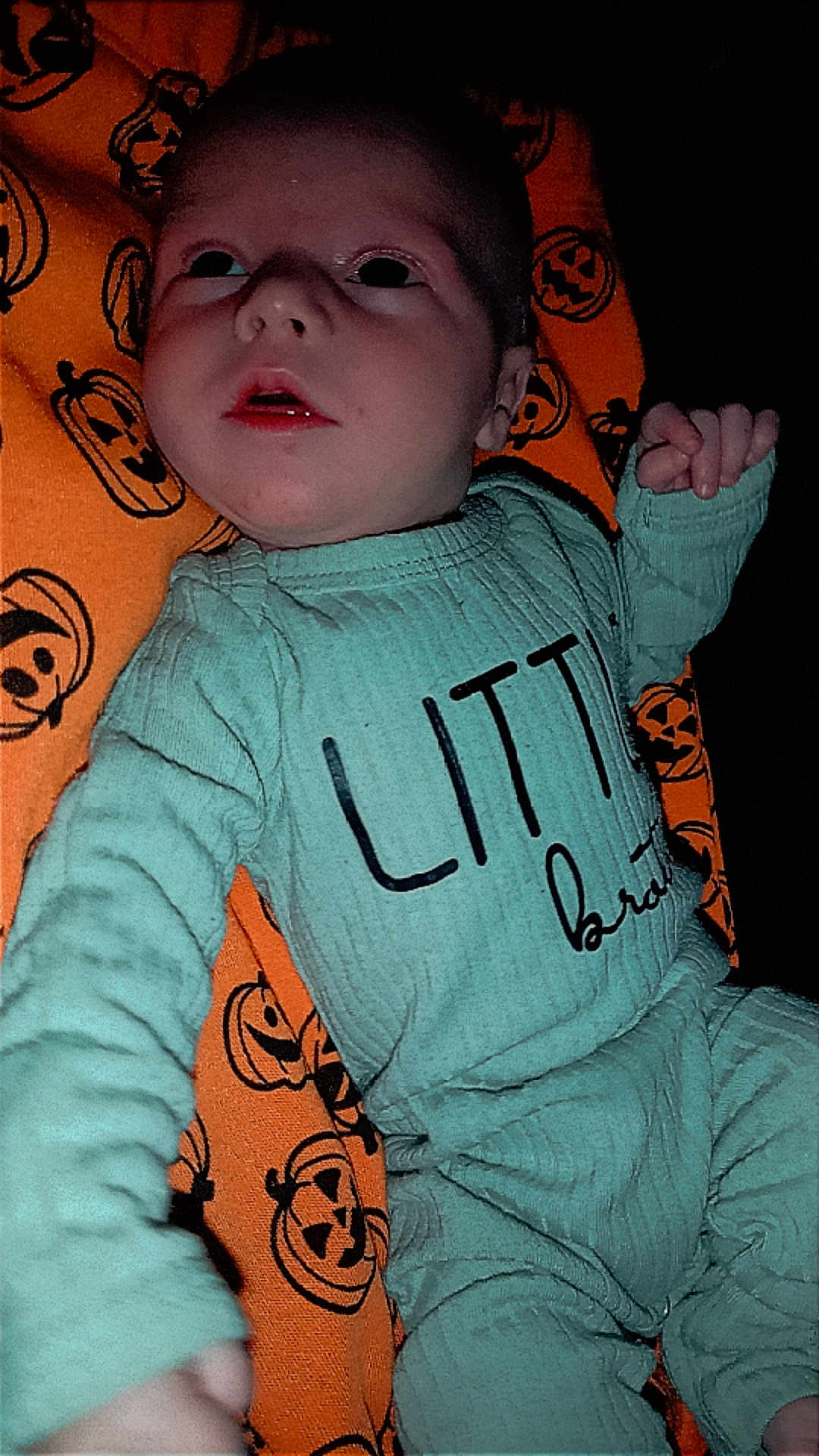 Braxton is registered to the contest to win money with this photo: baby, infant, child, clothing, green_outfit, blanket, orange_blanket, jack_o_lantern, pumpkin_pattern, face, hand, lying_down, cute, expression, indoors, portrait, young_child, sleepwear, fabric, person