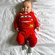 Axel joined the competition — help win amazing prizes! baby, bed, blanket, cartoon_print, child, comfort, cute, expression, face, indoors, infant, lying_down, person, portrait, red_clothing, sleepwear, socks, soft_light, tongue_out, white_sheet