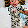 baby, child, onesie, spider, smile, happy, standing, bed, pillow, hand, foot, person, indoors, cute, infant, clothing, face, expression, support, home