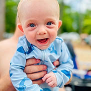 Kit is registered to the contest to win money with this photo: baby, child, blue_outfit, shark_print, smiling, happy, face, hands, person, closeup, portrait, outdoor, blurred_background, skin, infant, cute, joyful, bright_eyes, holding, human