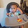 toddler, child, headphones, high_chair, toy, butterfly, indoor, carpet, vacuum_cleaner, door, bag, floor, wall, clothing, person, baby, expression, seat, tray, curious