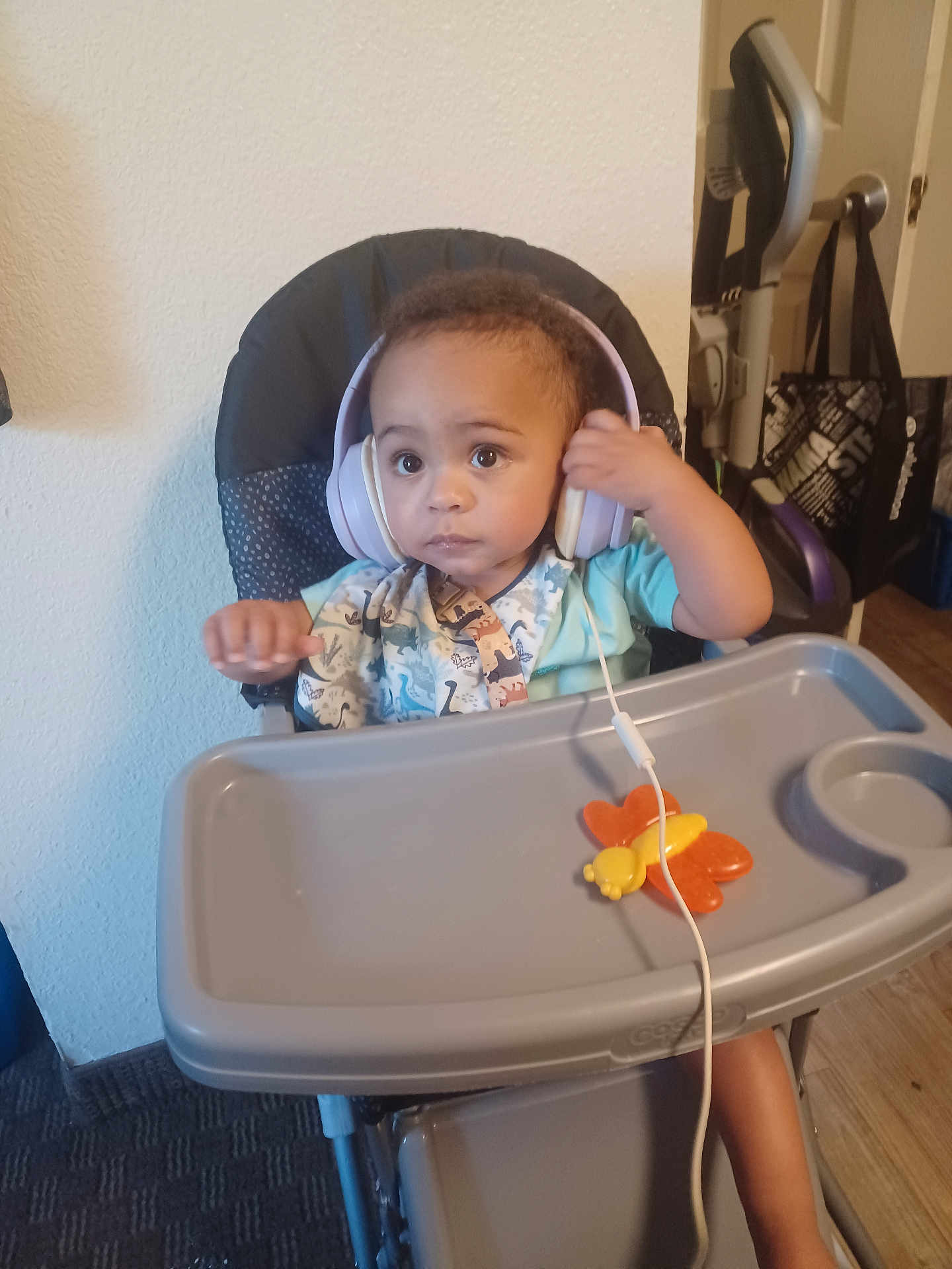 Azrael joined the competition — help win amazing prizes! toddler, child, headphones, high_chair, toy, butterfly, indoor, carpet, vacuum_cleaner, door, bag, floor, wall, clothing, person, baby, expression, seat, tray, curious