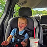 toddler, child, car_seat, car_interior, blue_shirt, smiling, laughing, drink, red_straw, seatbelt, window, trees, daylight, vehicle, happy, person, safety, transportation, cute, casual
