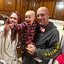 Seth is registered to the contest to win money with this photo: baby, child, adult_male, adult_female, family, kitchen, wooden_cabinets, plaid, pajamas, hoodie, glasses, smile, holding, pointing, excited, indoor, stove, bathrobe, portrait, cozy