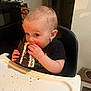 child, toddler, baby, cake, chocolate_cake, eating, highchair, crumbs, frosting, messy, hands, face, portrait, indoor, kitchen, dining, tray, curious_expression, snack, candid