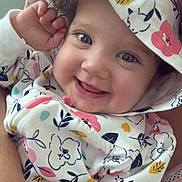 Samantha is registered to the contest to win money with this photo: baby, child, smile, hoodie, patterned_clothing, blue_eyes, curly_hair, cute, happy, portrait, indoor, closeup, infant, person, face, hand, floral_print, soft_lighting, childhood, warmth