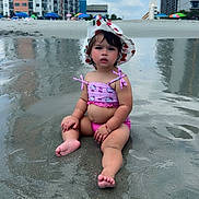 Daenerys is registered to the contest to win money with this photo: toddler, child, beach, sand, water, swimsuit, hat, sunhat, urban, buildings, umbrella, reflection, summer, outdoor, vacation, sitting, cute, baby, sky, clouds