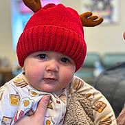 Bellamie is registered to the contest to win money with this photo: baby, child, red_hat, antlers, knit_hat, onesie, breakfast_pattern, hand, blanket, indoor, portrait, cute, soft_focus, face, person, infant, warm_clothing, expression, holding, cozy