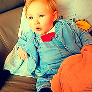 Yzïa a rejoint le concours — aidez-le/la à gagner de superbes lots ! baby, blanket, blond_hair, blue_eyes, casual_clothing, child, colorful_background, curious_expression, cushion, denim_jacket, hand, indoor, legs, pacifier, ponytail, portrait, red_bow, sofa, soft_lighting, toddler