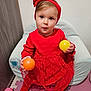 toddler, child, red_dress, headband, ball, yellow_ball, orange_ball, pink_ball, cushioned_chair, play_mat, indoor, curious_expression, blue_eyes, sitting, soft_furniture, floor_mat, baby, playful, cute, portrait