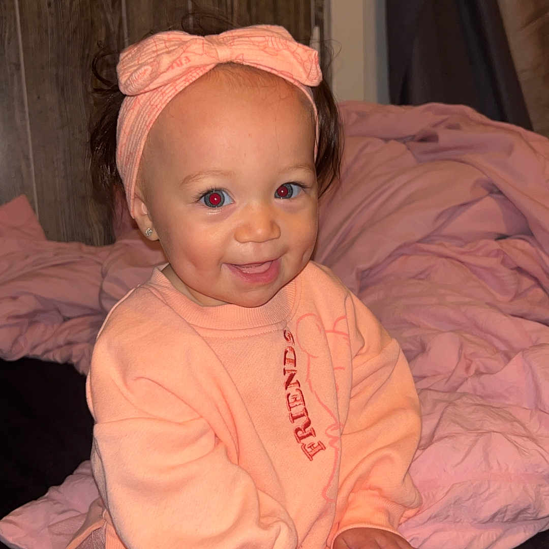 Reignmarie joined the competition — help win amazing prizes! baby, bed, blanket, bow, child, clothing, cute, face, hand, happy, headband, indoor, leggings, person, pink, sitting, smiling, sweatshirt, toddler, wooden_wall