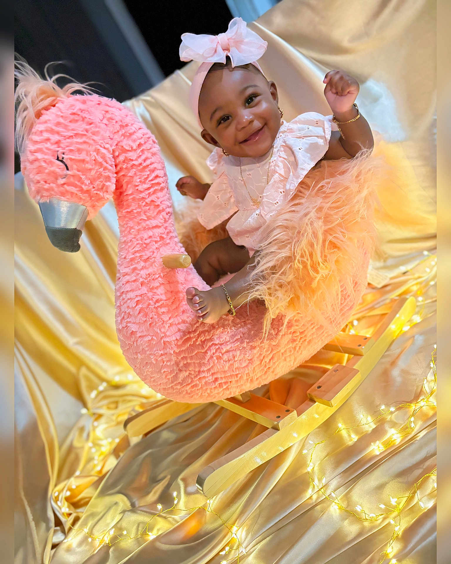 Sayuri joined the competition — help win amazing prizes! baby, child, smiling, pink_bow, flamingo, rocking_horse, plush_toy, golden_satin, fairy_lights, jewelry, cute, happy, portrait, indoor, soft_texture, decorative_lighting, infant, adorable, headband, playful