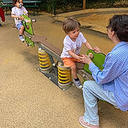 Axel Et Leo a rejoint le concours — aidez-le/la à gagner de superbes lots ! adult, bench, casual_clothing, child, children, footwear, greenery, happy, interaction, outdoor, pacifier, playground, playing, sandpit, seesaw, shorts, smiling, spring, toy, tshirt