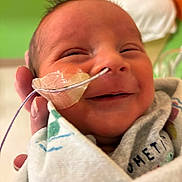 Bobby Ray Coca Iii is registered to the contest to win money with this photo: newborn, baby, smile, face, nasal_tube, hospital, blanket, infant, hand, medical_tape, swaddled, healthcare, person, closeup, cute, head, sleepy, skin, young_child, indoors