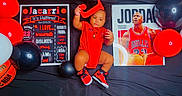 Jacarri is registered to the contest to win money with this photo: baby, balloons, basketball, black_background, child, clothing, football, letter_j, michael_jordan, nba, person, poster, red_clothing, red_shoes, sneakers, sports, text_board, toy, white_balloon, young_child