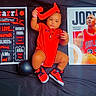 baby, balloons, basketball, black_background, child, clothing, football, letter_j, michael_jordan, nba, person, poster, red_clothing, red_shoes, sneakers, sports, text_board, toy, white_balloon, young_child