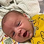baby, infant, yellow_clothing, blanket, patterned_blanket, face, head, skin, eyes, mouth, lying_down, indoors, cute, newborn, child, person, happy, expression, soft, comfort