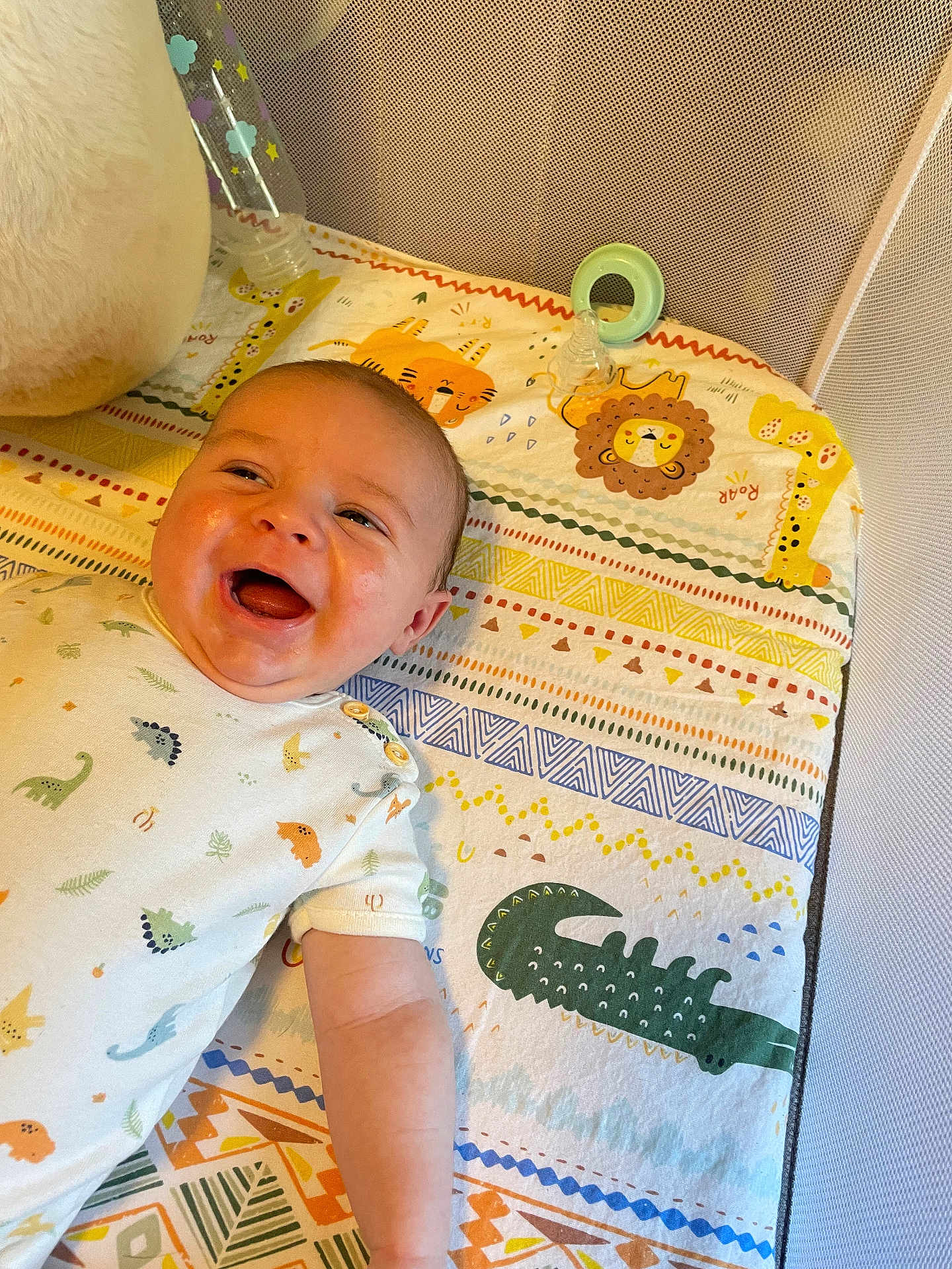 Elijah joined the competition — help win amazing prizes! baby, infant, smiling, happy, play_mat, animal_print, lion, giraffe, crocodile, colorful, cute, child, clothing, onesie, lying_down, indoor, face, skin, joyful, adorable