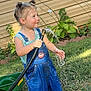 Raelynn Thrasher is registered to the contest to win money with this photo: boots, child, fun, garden, grass, green, happy, hose, outdoor, overalls, pigtails, plants, play, smiling, splash, sunlight, toddler, water, wheelbarrow, yard