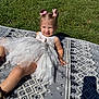 Raelynn Thrasher joined the competition — help win amazing prizes! blanket, child, cute, daylight, dress, fun, grass, hair_bows, happy, outdoor, patterned_blanket, playful, portrait, sitting, smiling, summer, sunlight, toddler, white_dress, young_child
