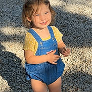 Raelynn Thrasher is registered to the contest to win money with this photo: blue_eyes, car, casual_clothing, child, cute, daylight, denim_overalls, gravel, happy, outdoor, person, sandals, shadow, short_hair, small_child, smiling, standing, sunlight, toddler, yellow_shirt